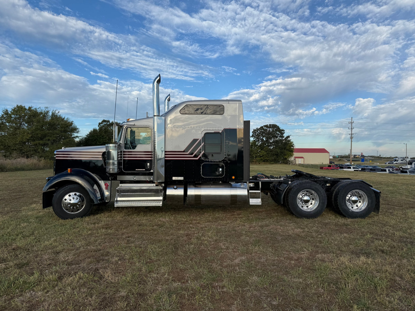 Kenworth W900L conventional sleeper truck side view showing dual rear axles, chrome exhaust stacks, and custom sleeper cab with black and silver livery.