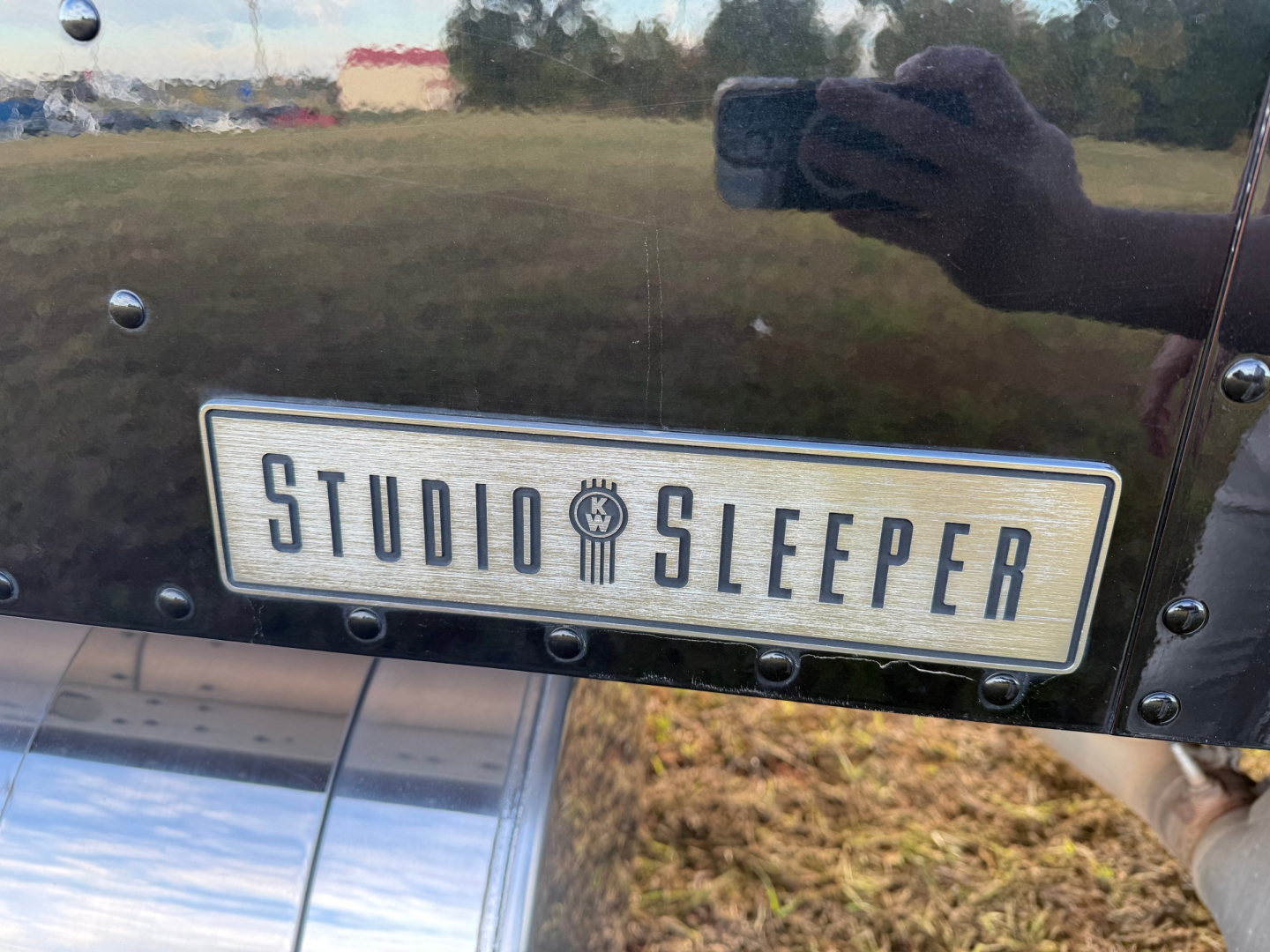 Kenworth W900L cab side showing Studio Sleeper badge and reflection of photographer with phone.