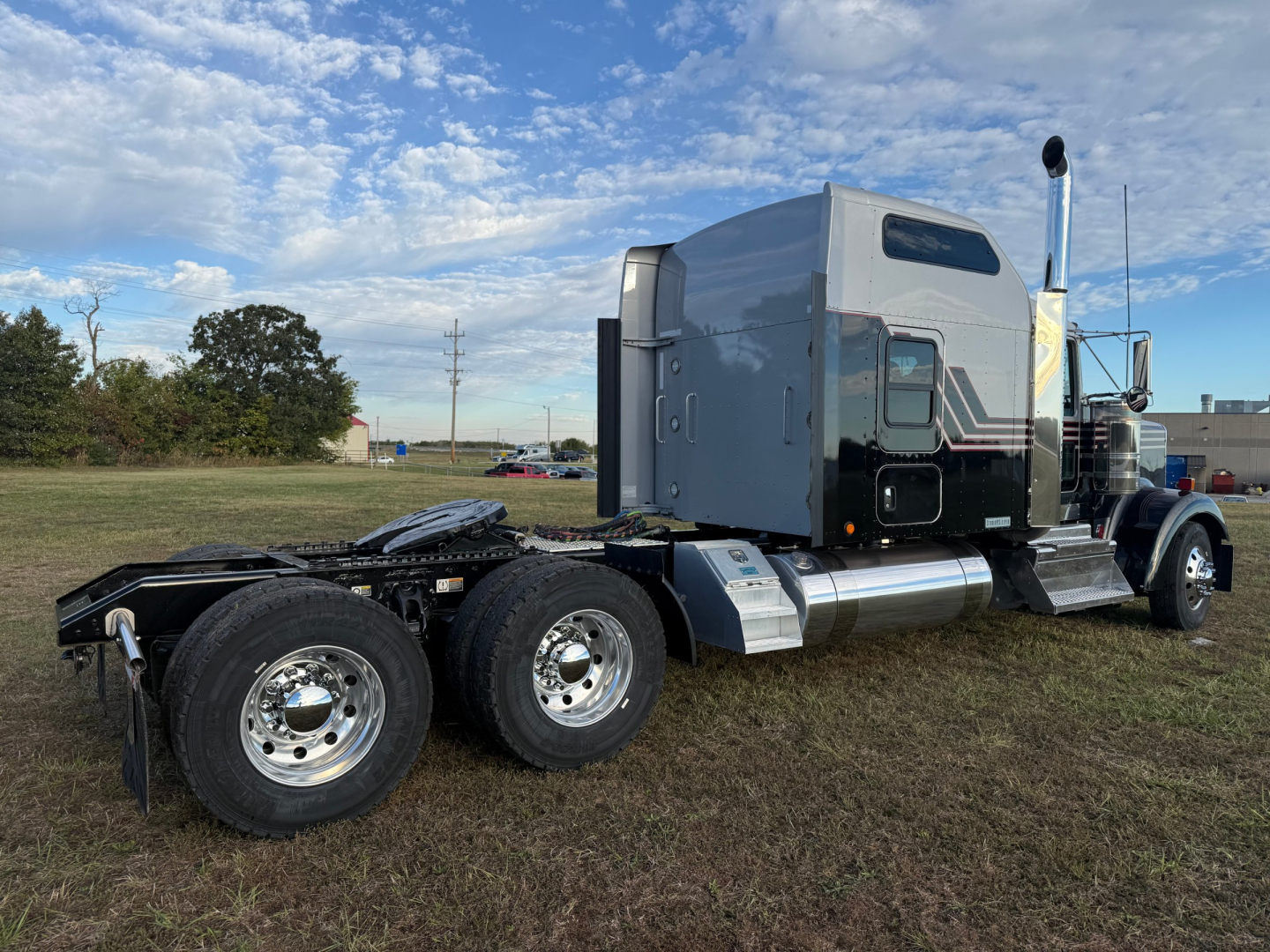 Kenworth W900L tractor conv sleeper truck side view showing dual rear axles, chrome fuel tanks, and silver aerodynamic sleeper cab with black stripe accents.