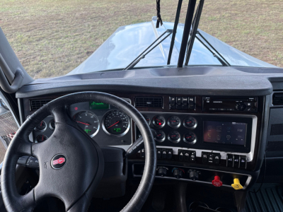 Kenworth W900L cab interior showing steering wheel, instrument cluster, and dashboard controls with gauges and digital display
