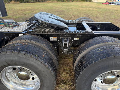 Kenworth W900L chassis rear view showing dual rear axles with large dual tires, chrome wheels, fuel/brake system fittings, and a circular hitch/spare carrier on a flatbed frame.