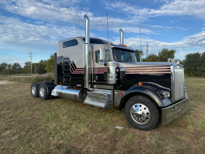 Kenworth W900L conventional sleeper truck in a grassy lot with chrome exhaust stacks and polished chrome bumper, black with red pinstriping.