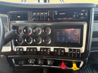 Kenworth W900L dash panel with multiple gauges, aftermarket infotainment touchscreen, Kenworth radio, and toggle switches.
