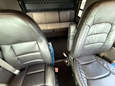Cab interior of a Kenworth W900L truck showing two front seats, center console, seat belts, and rear cabin seating with leather upholstery.