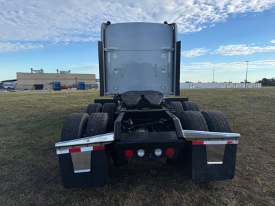 Kenworth W900L rear view showing fifth wheel, dual rear axles, and mud flaps; back of cab with vertical exhaust stacks and taillights visible.
