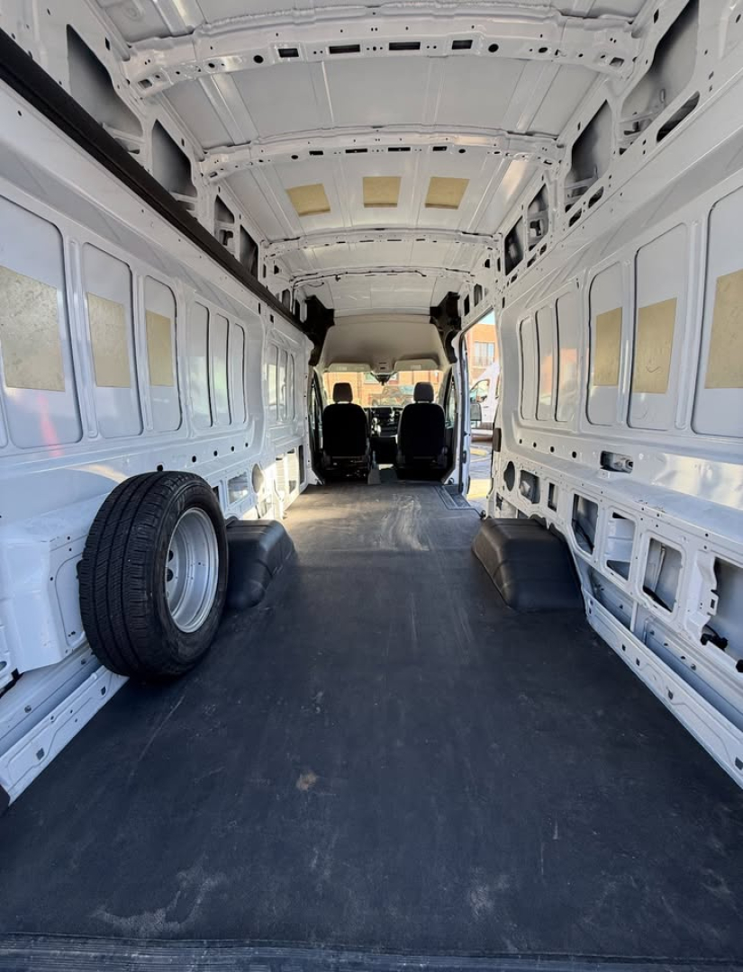 Ford Transit 350 HD cargo van interior empty cargo area with wheel on left, two front seats visible, metal walls and ceiling, no shelving.