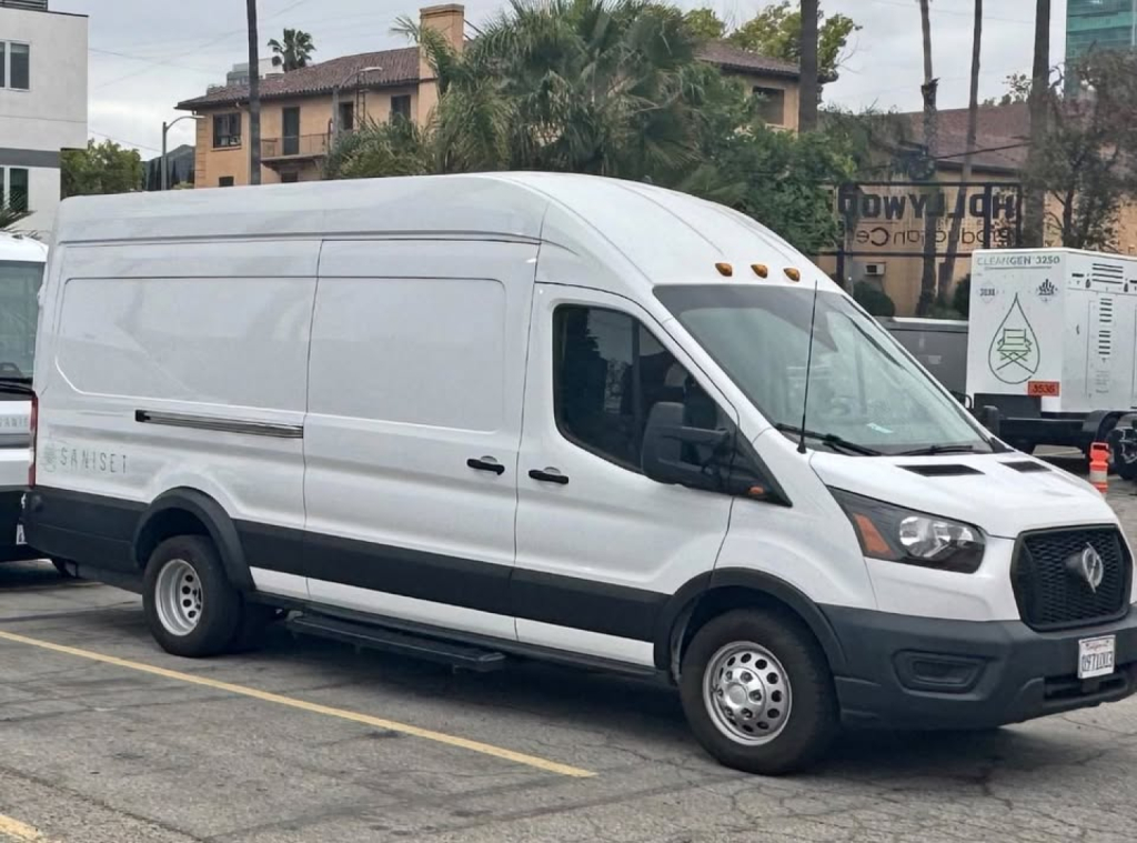 Ford Transit 350 HD cargo van in white, side view with raised roof, black bumper, and dual rear wheels. VIN partially visible on plate, parked in lot.