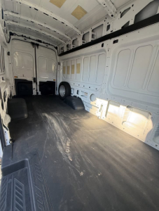 Transit cargo van interior showing empty cargo area with white panel walls and black rubber flooring.
