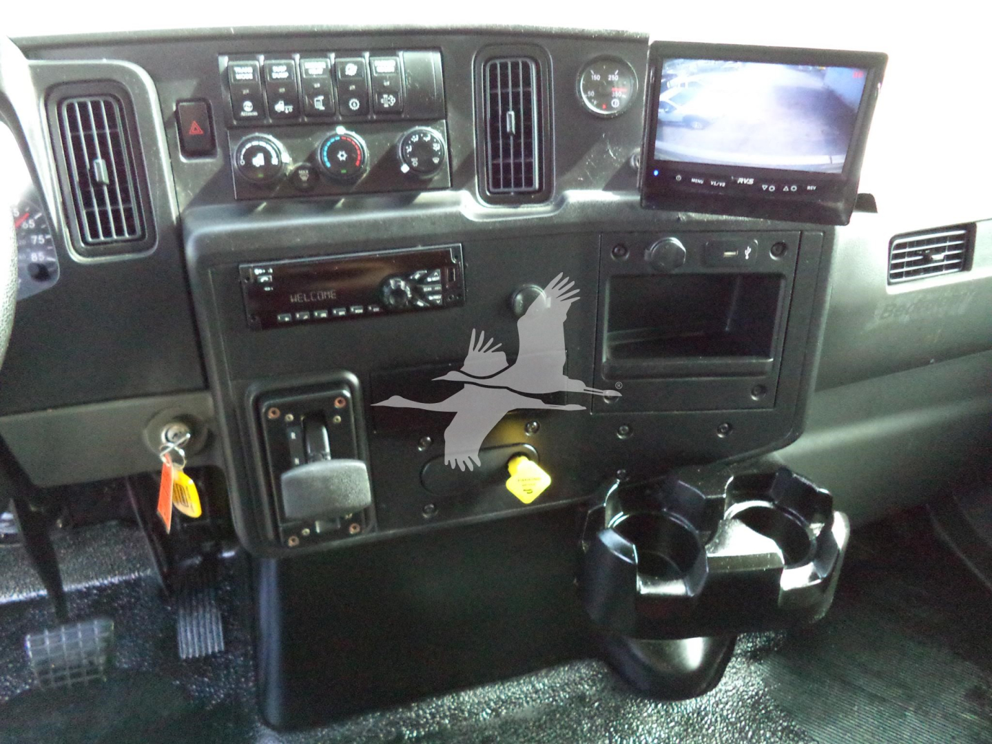 Truck cab interior showing dashboard with control panel, infotainment screen, gauges, cup holders, and gear shifter.