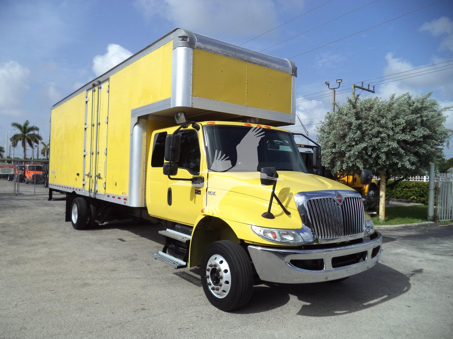 Box truck side view showing a bright yellow cargo box and front cab, International logo on grille, large side mirrors, undercarriage and wheel details visible.