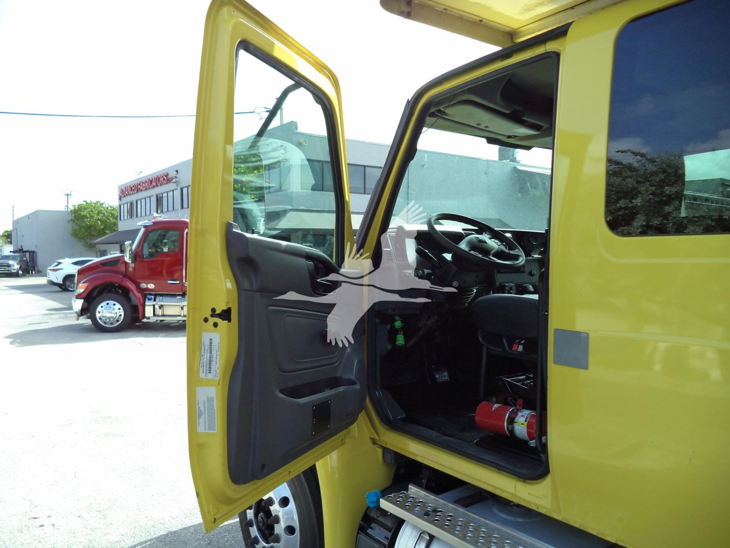 Truck cab interior showing open door of a yellow 2020 International MV moving van with steering wheel and dashboard visible