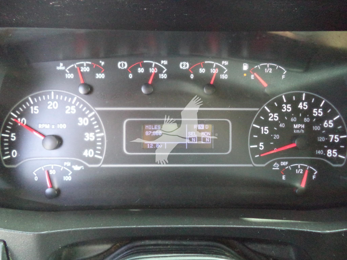 Dashboard gauge cluster from a 2020 International MV showing multiple analog gauges and a center digital readout with faint overlay. Visible text includes MPH/kmh scale on left/right, fuel gauge, engine oil, coolant, and other indicators.