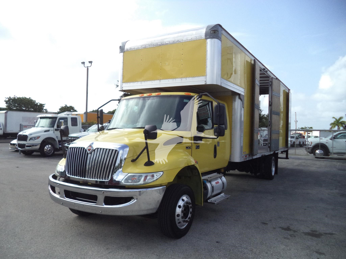 Yellow International MV moving van truck in a dealership lot, cab with chrome grille and rectangular cargo body; VIN and stock not visible in image.