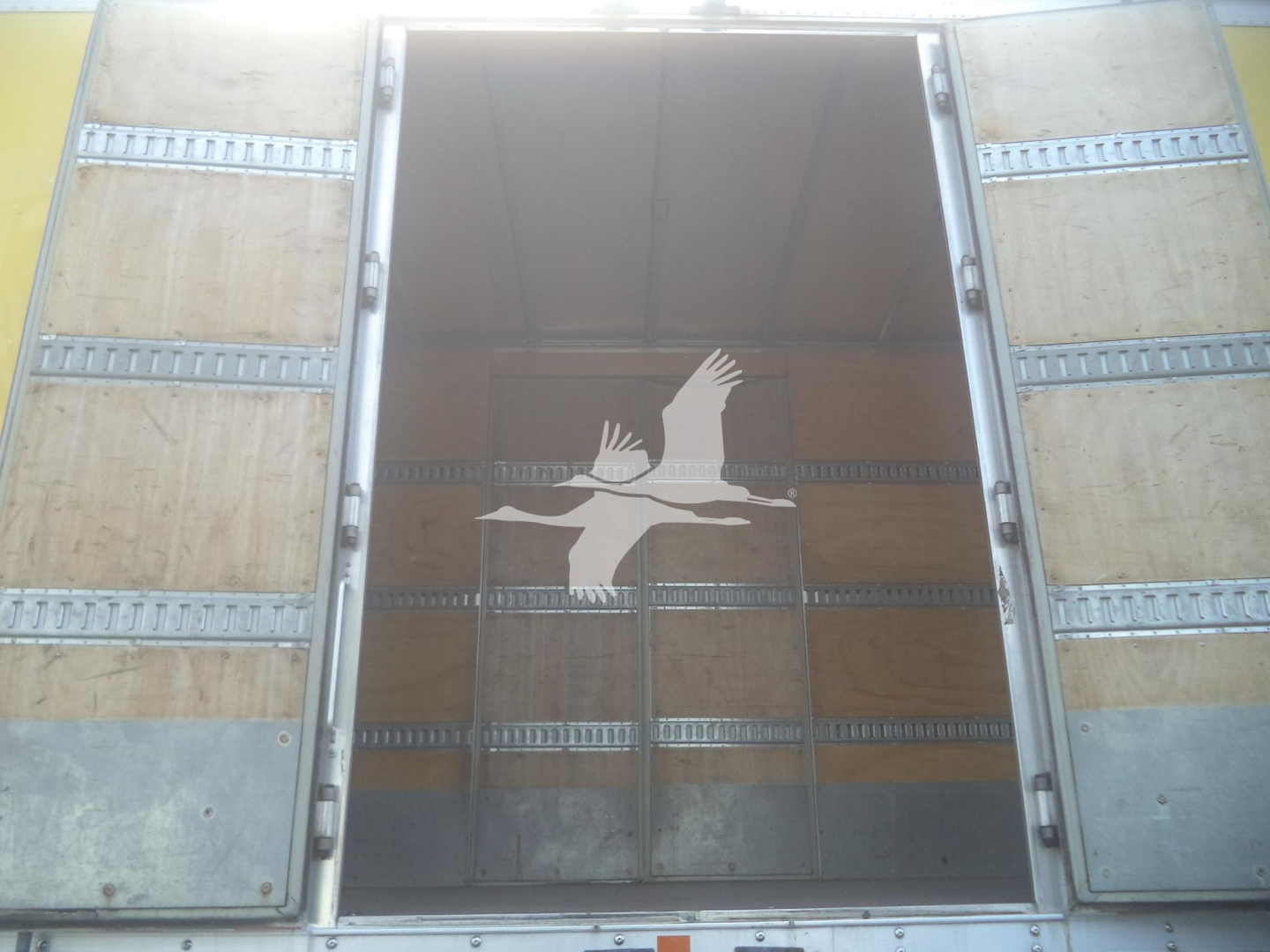 Truck trailer back opening showing empty cargo area with metal frame and wooden interior.