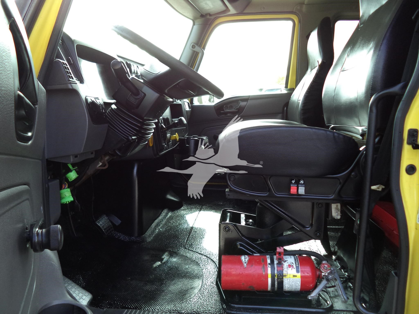 Truck cab interior showing steering wheel, dashboard, and seat with a fire extinguisher on the floor near the driver's door.
