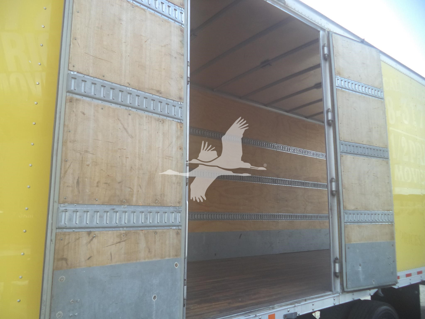 Truck cargo area open with wooden walls and metal rails, interior empty, side doors open, yellow exterior panels visible.