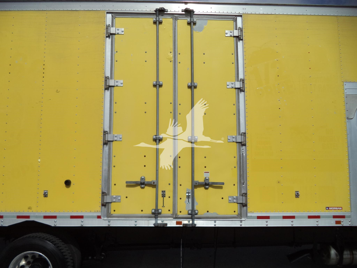 Truck body side showing yellow moving van with white bird logo and rear double doors, metal latches and hinges visible.