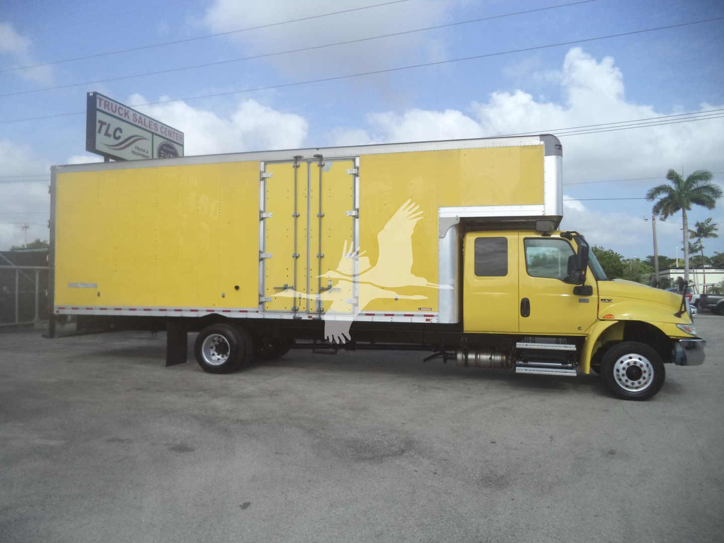 Truck side view: yellow moving van/box truck with extended cargo area and steps, International logo on cab, no visible text other than stock unit features.