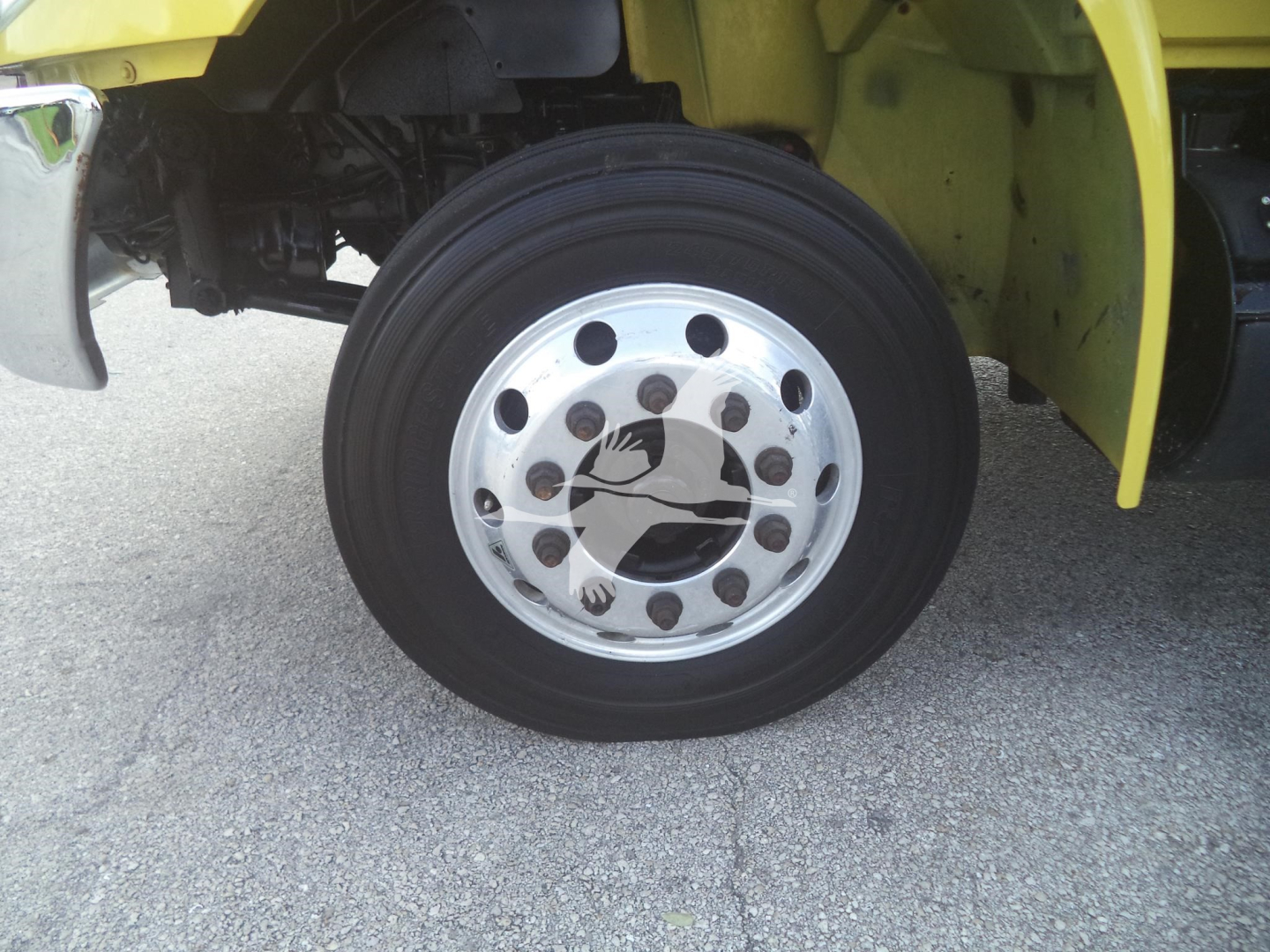 Wheel and tire of a yellow moving van with chrome hubcap and multiple lug nuts visible.