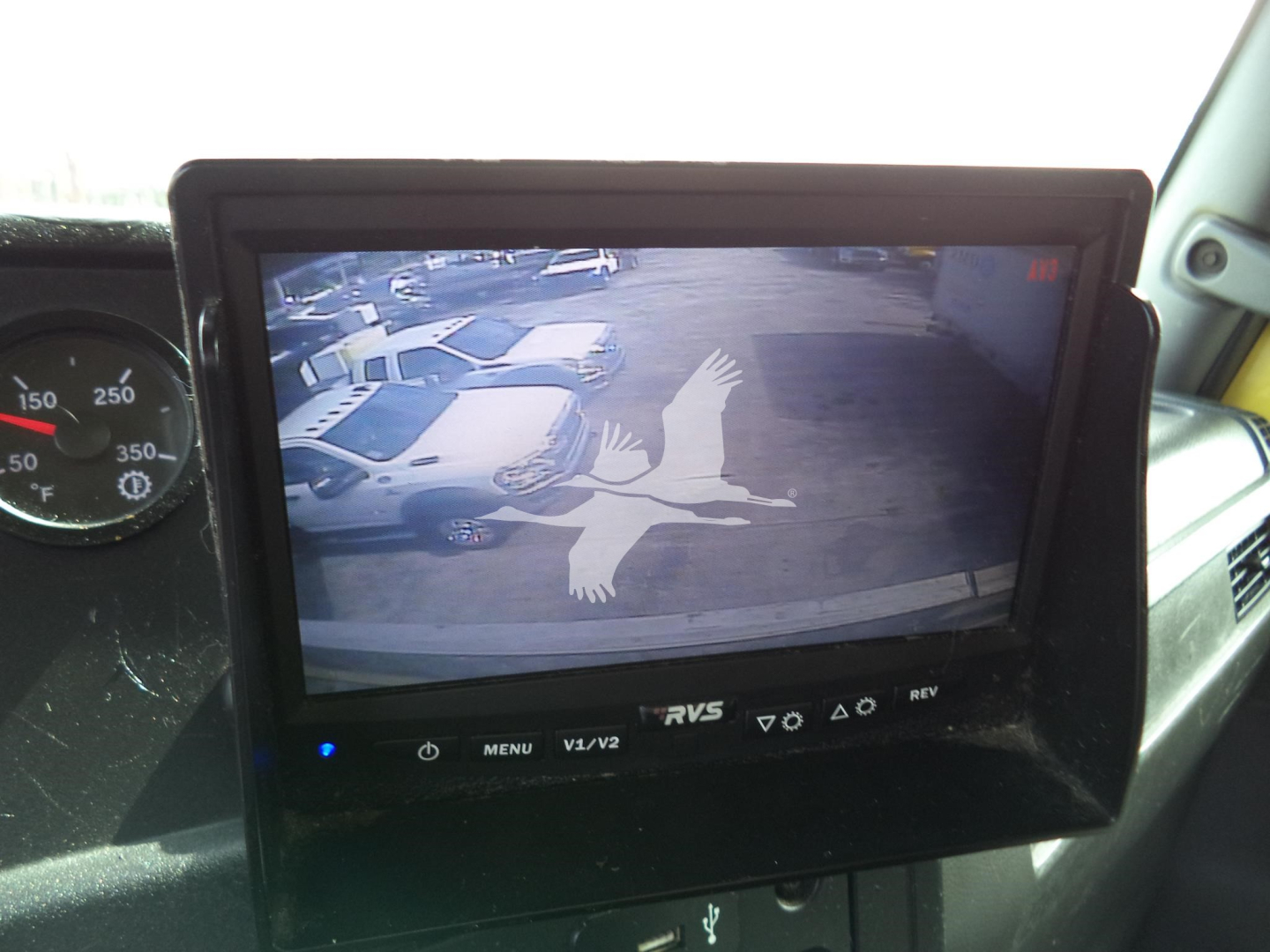 In-cab monitor displaying a bird logo on a rear-view camera screen; surrounding dashboard with gauge cluster visible.