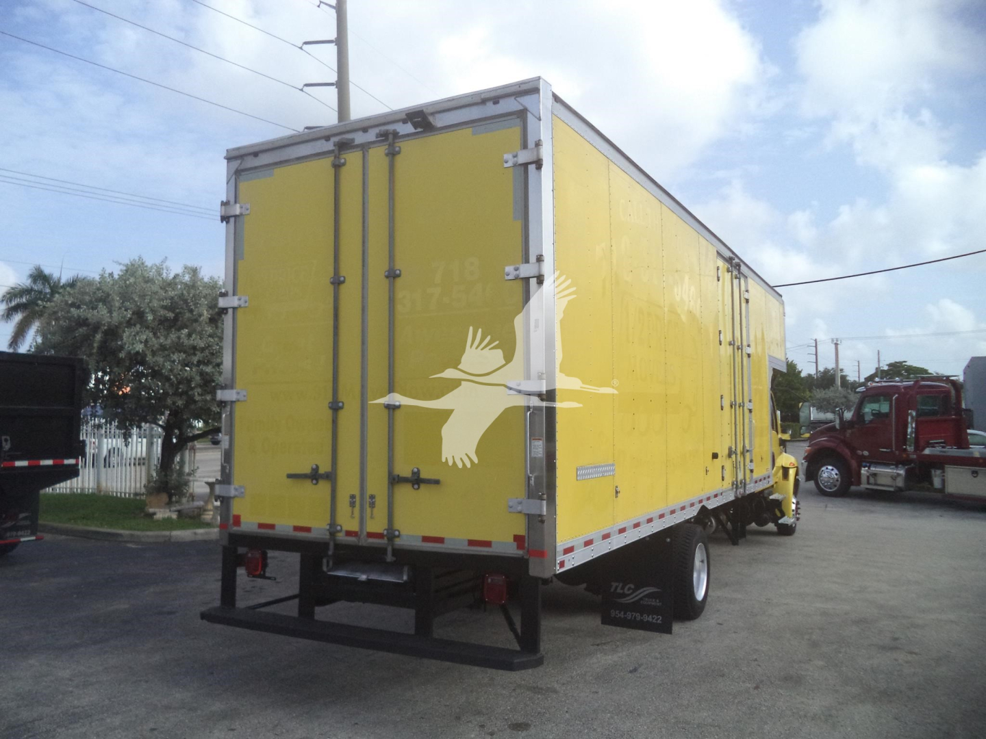 Yellow cargo box truck trailer with rear double doors showing metal latches, white bird graphic on doors, and reflective tape along edges; black bumper and wheel wells visible.