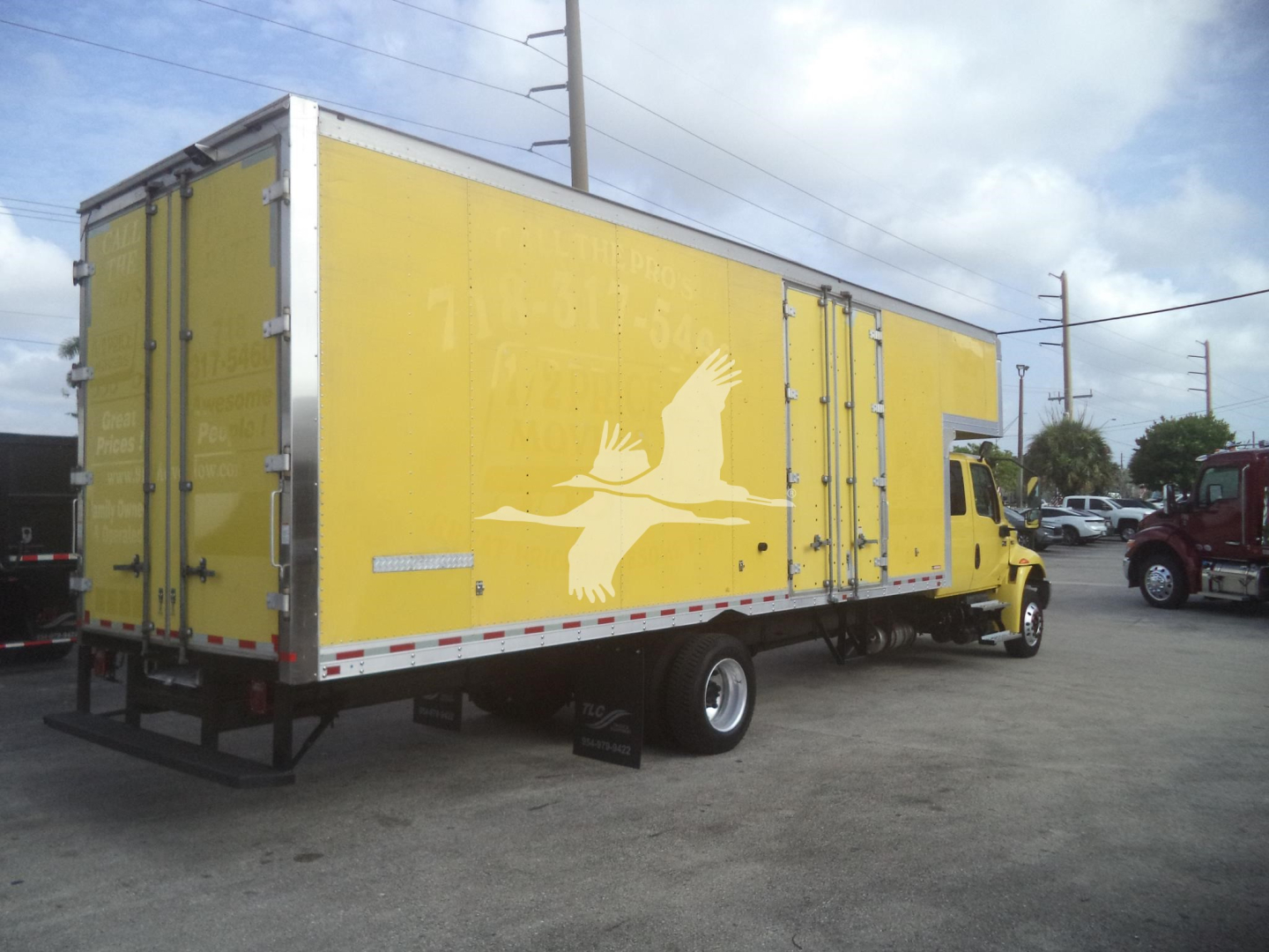 Yellow moving box truck with a white bird logo on the side, viewed from rear-left, cargo area doors closed.