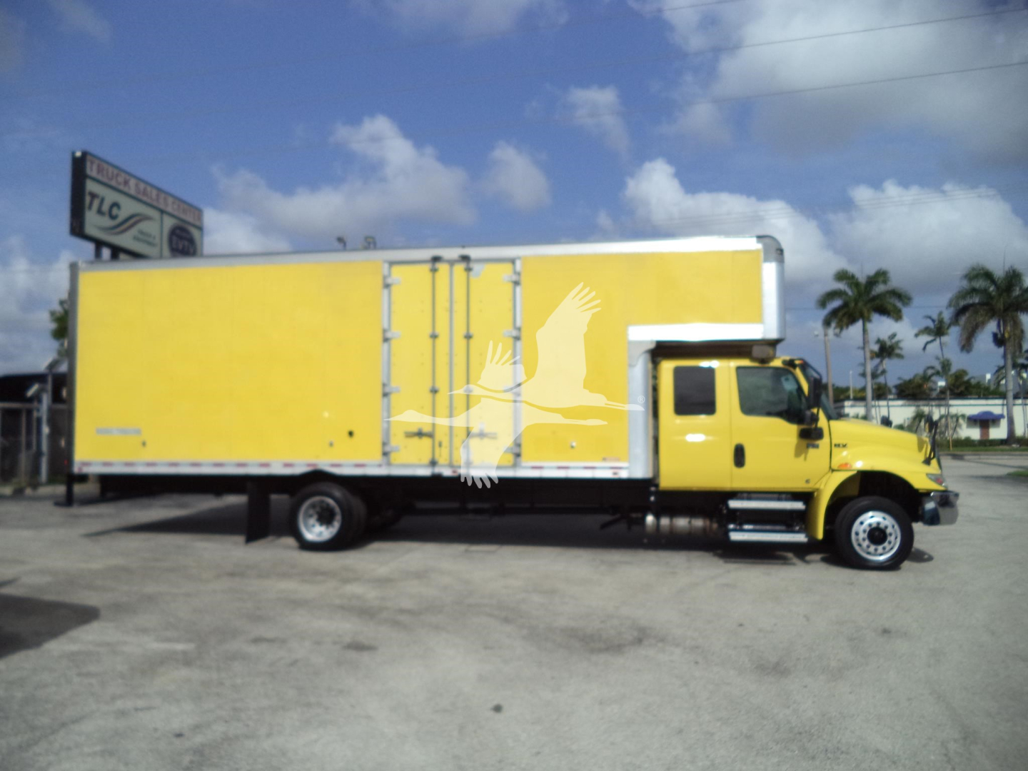 Yellow moving van truck side view with cargo box behind cab showing white graphic bird and palm trees on side.