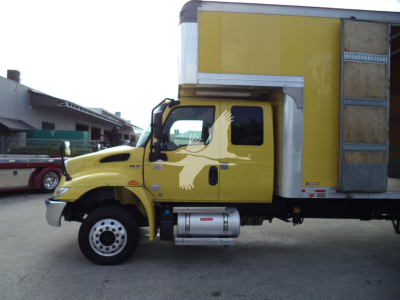 Truck cab and cargo box of a yellow 2020 International MV moving van, side view showing front wheel, fuel tank, and cargo box with wooden panel door.
