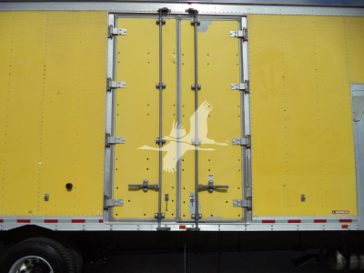 Truck body side showing yellow moving van with white bird logo and rear double doors, metal latches and hinges visible.