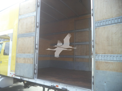 Interior of a moving van with open rear doors; wooden walls with metal rails and a white bird decal on the far wall.