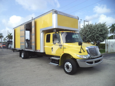 Yellow and gray moving van truck with open cargo area and rear ramp, International front end, clear sky