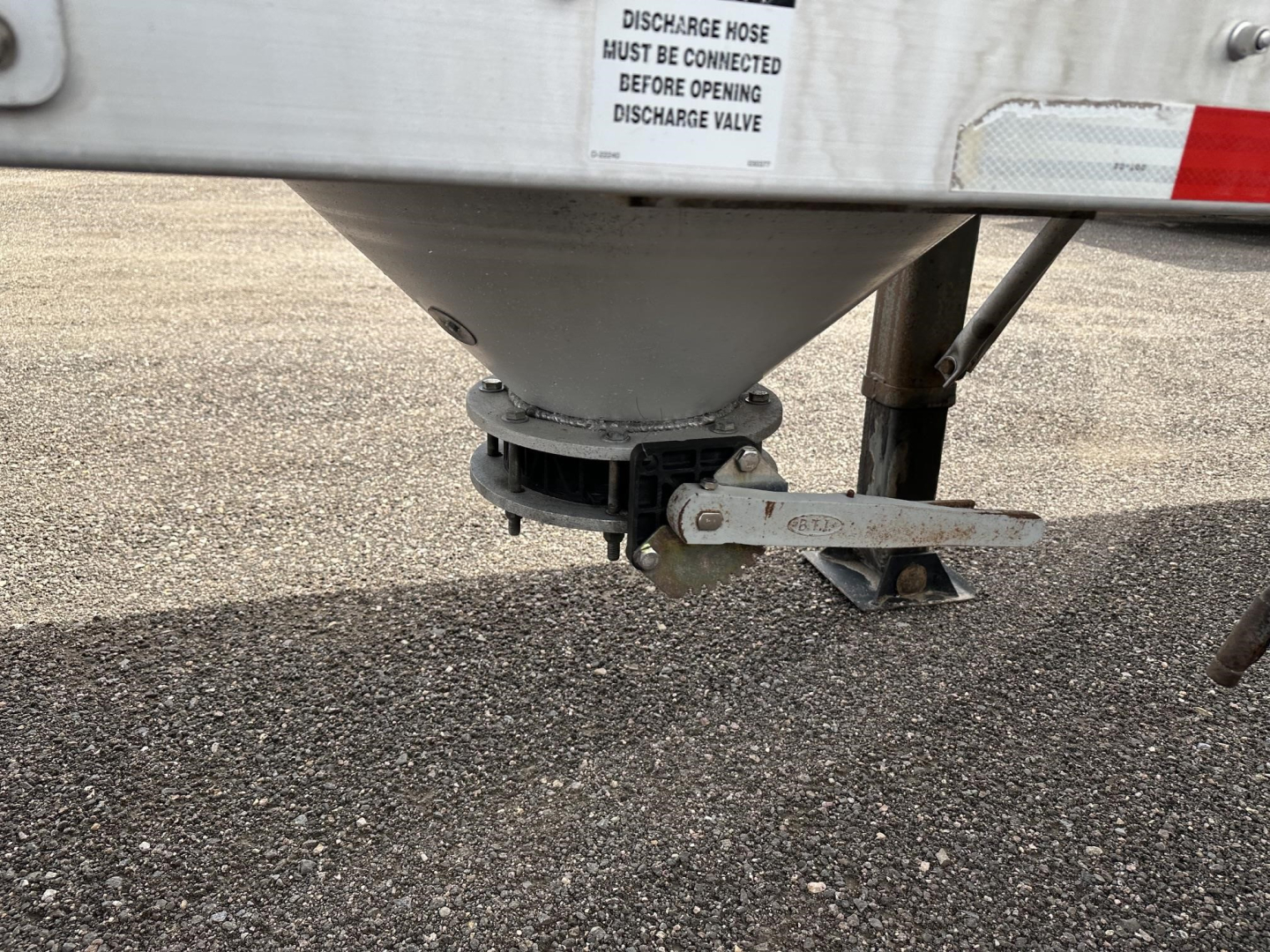 Trailer underside showing discharge valve and hitch on a Polar Gravity Drop pneumatic trailer. Text on label: DISCHARGE HOSE MUST BE CONNECTED BEFORE OPENING DISCHARGE VALVE.