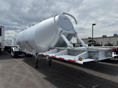 Polar gravity drop pneumatic trailer showing cylindrical tank and rear loading mechanism with support legs and hitch in an outdoor lot.