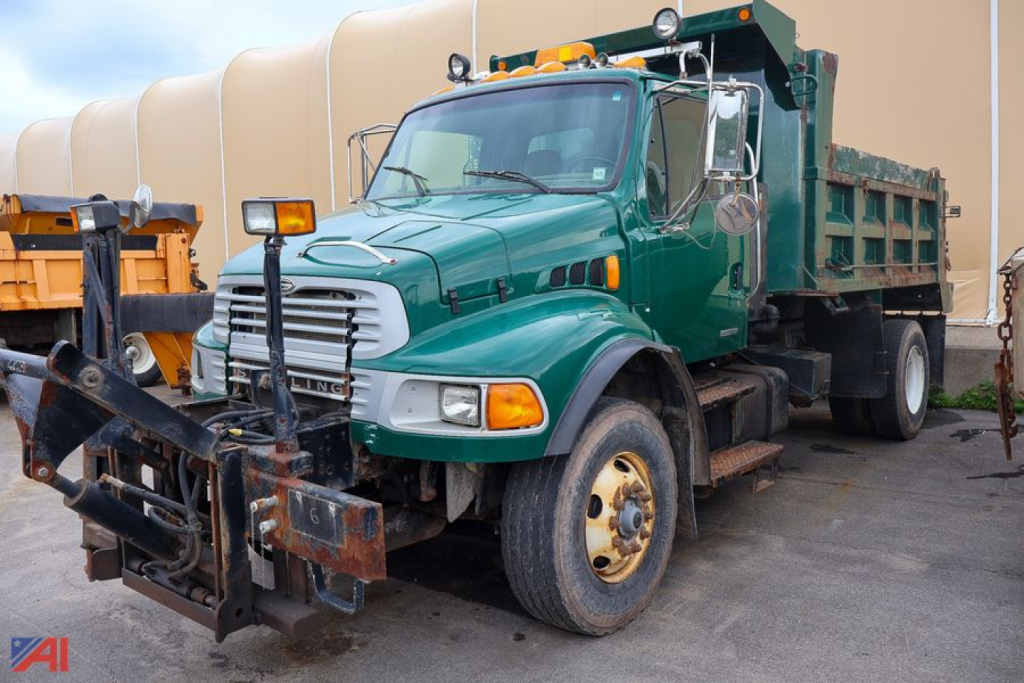 Green Sterling Acterra dump truck with front-mounted snow plow attachment, cab-facing view, showing dump bed and side mirrors.