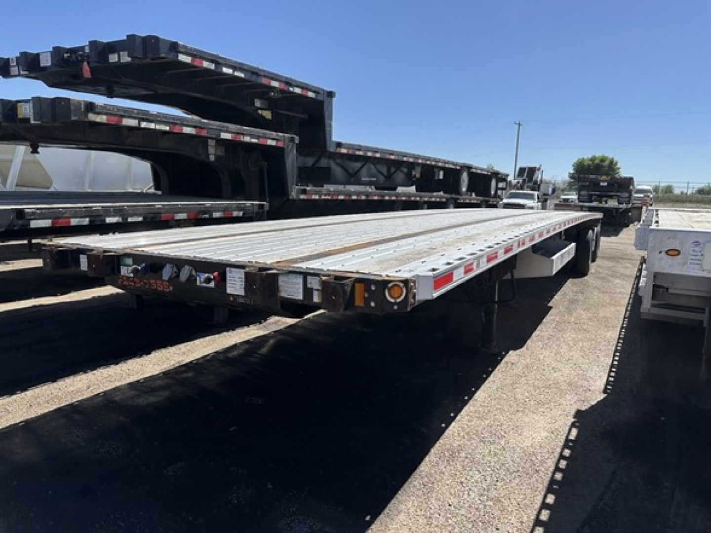 Flatbed trailer in a lot showing long aluminum deck and tandem axles with reflective tape and attach points.