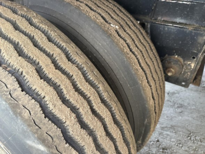 Trailer tire with dual wheels and stacked treads; gravel and dirt on tire surface; part of Fontaine Infinity flatbed trailer.