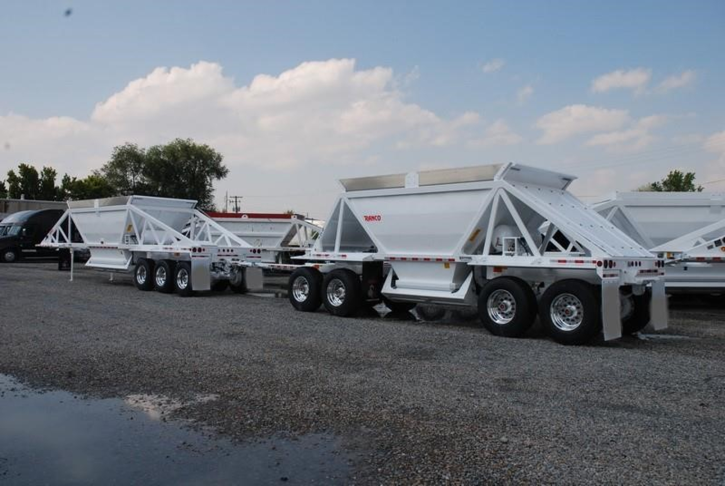 Rear view of a line of white bottom-dump trailers with triple-axle configurations, showing clean metal frames and tail gates.