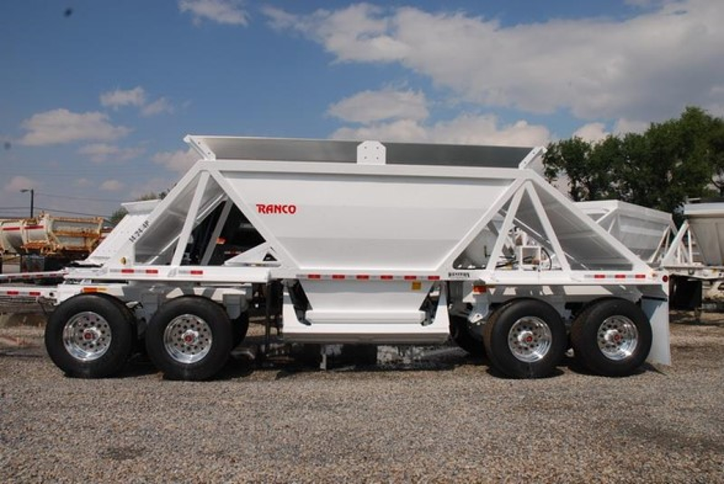 Bottom dump trailer showing white Ranco logo and dual-axle tandem wheels, with a raised tipping hopper and metal frame.