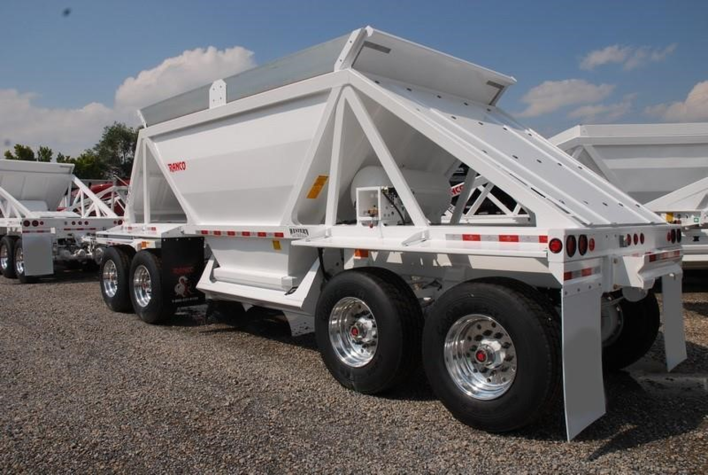 Rear/side view of a white Ranco light weight bottom dump trailer showing dual tandem axles and dumping hopper.