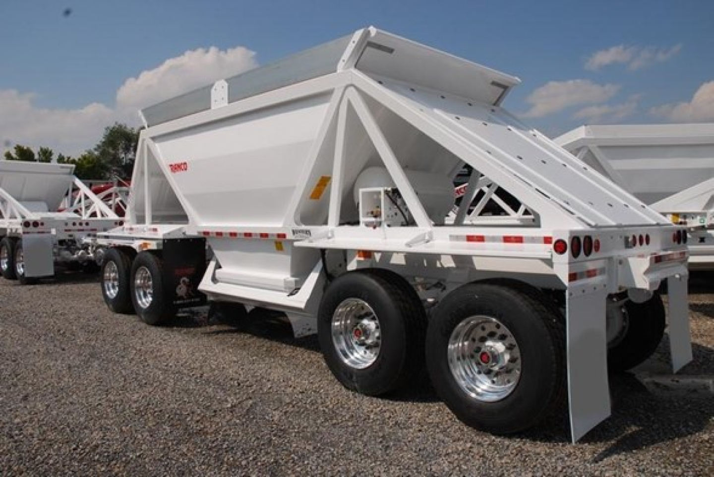 Bottom-dump trailer showing white Ranco lightweight bottom-dump trailer with dual rear axles and a folded dumping bed.