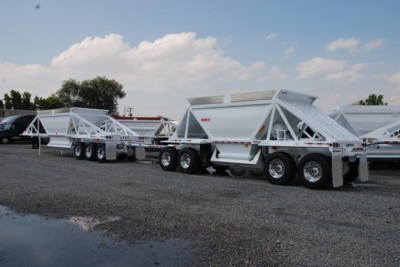 Lightweight bottom-dump trailers lined up in a lot, multiple axles, white metal frames with dump boxes.