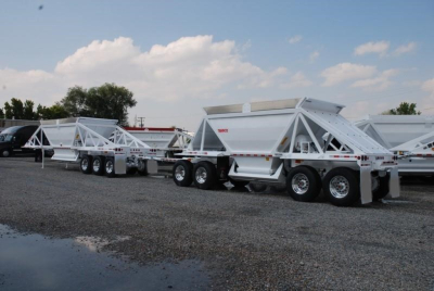 Rear view of a line of white bottom-dump trailers with triple-axle configurations, showing clean metal frames and tail gates.