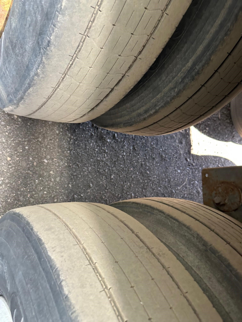 Trailer tire close-up showing dual tires with light tan tread and wear lines; part of wheel well and edge of trailer frame visible.