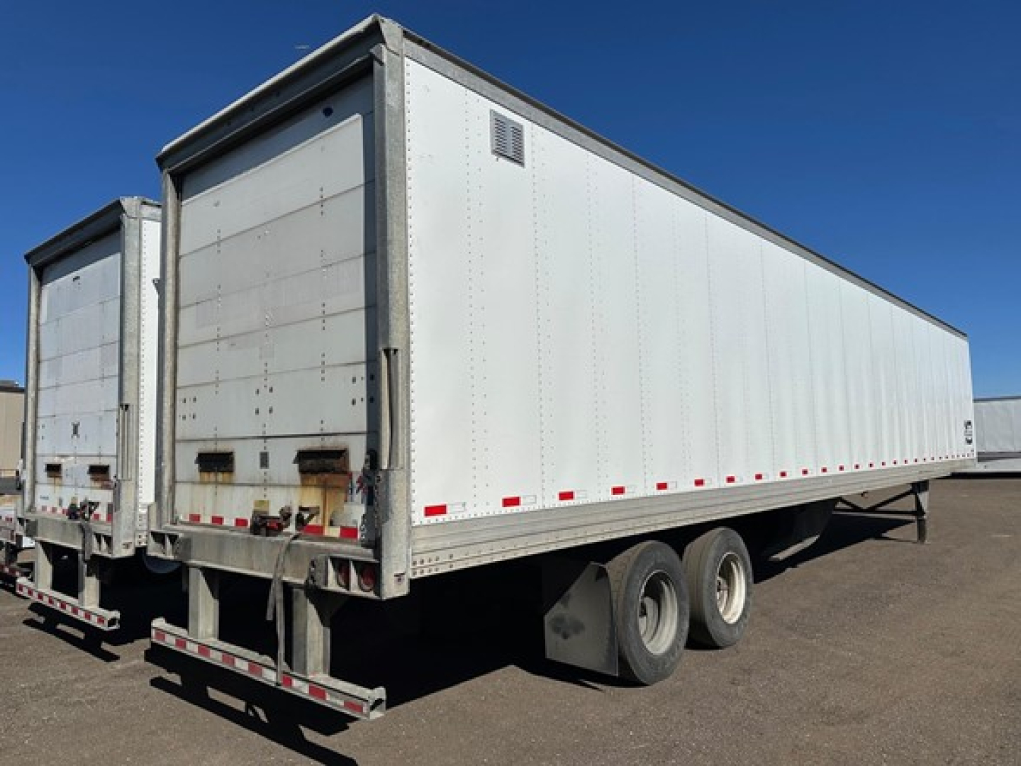Trailer side view showing a white Hyundai air ride dry van trailer with dual rear doors and roll-up door, undercarriage wheels visible.