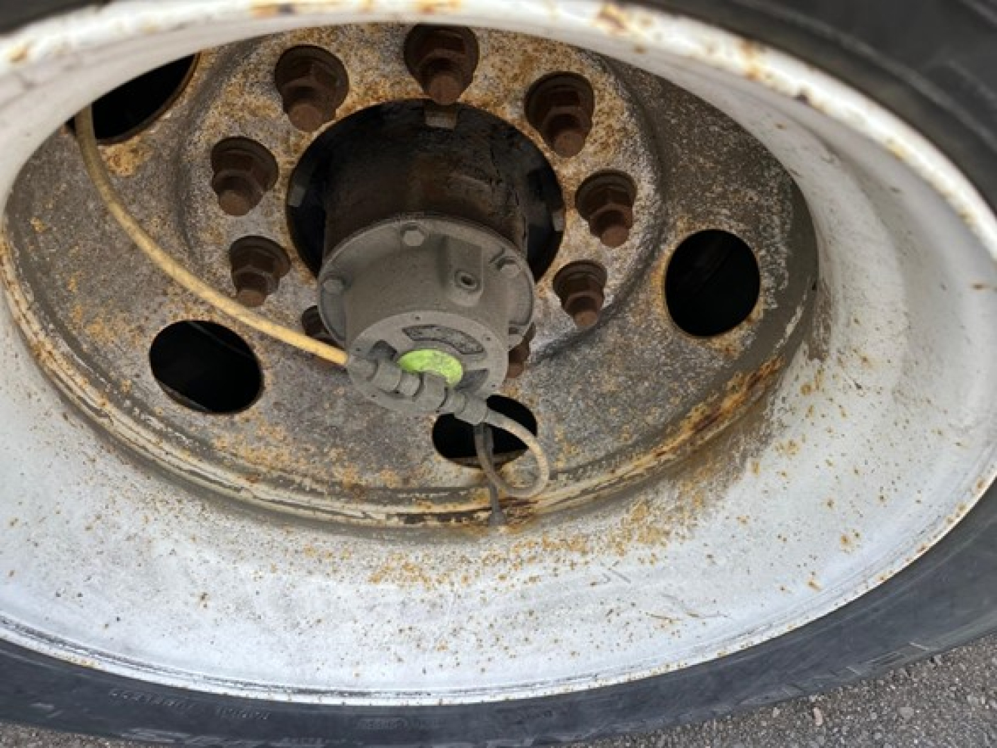 Wheel of a used Hyundai trailer showing rusted rim and hub with lug holes and a green valve cap.