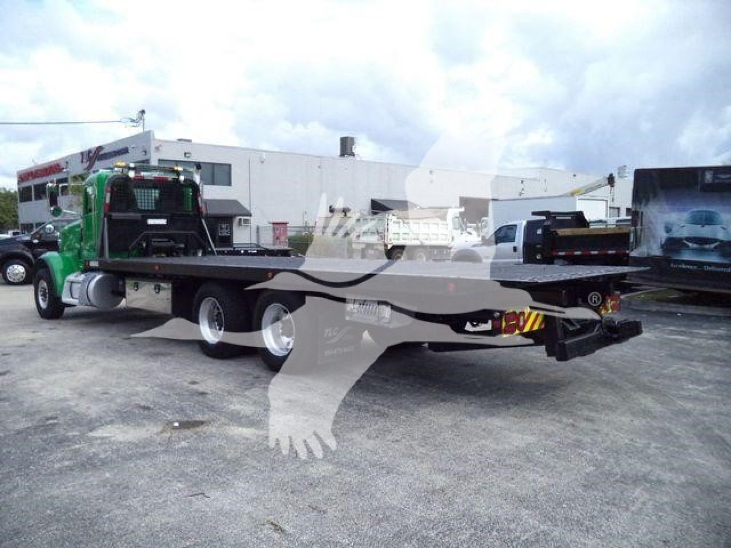 Truck bed with rollback flatbed and rear view showing equipment and trailer hitch. Visible text on the truck: none legible; logo watermark over image.