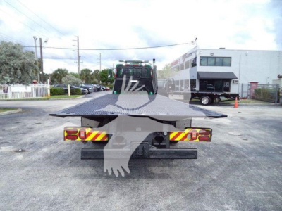 Back view of a 2014 Peterbilt 367 rollback truck with flatbed; lot in background with building and other vehicles.