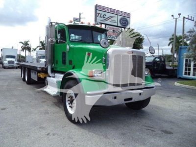 Peterbilt 367 tow truck, green and white, front view, large grille, chrome bumper, flatbed in background.