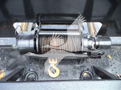 Winch mounting assembly with steel cable drum and hook on a trailer hitch, undercarriage view.