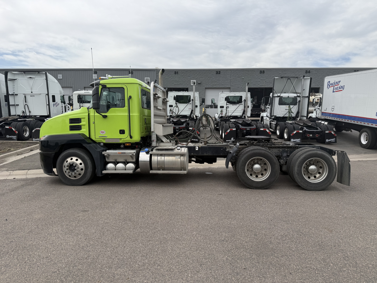 Truck chassis showing a lime-green Mack AN64T day cab with long wheelbase and dual rear axles, cab-forward design, side view in lot.